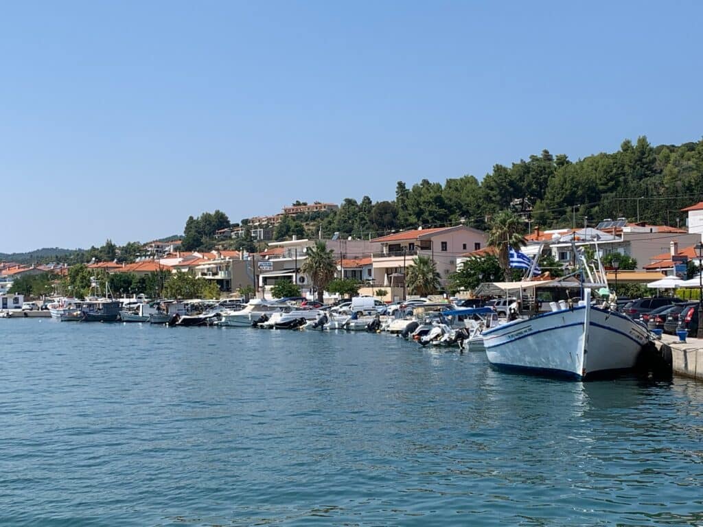 Coastal view of Halkidiki Green with small boats and a village of homes behind them just at the waters edge.