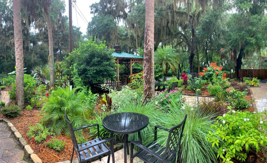 Garden at Hotel in Crystal River with a wrought iron black patio set sitting amongst lush greenery in a garden area for guests.