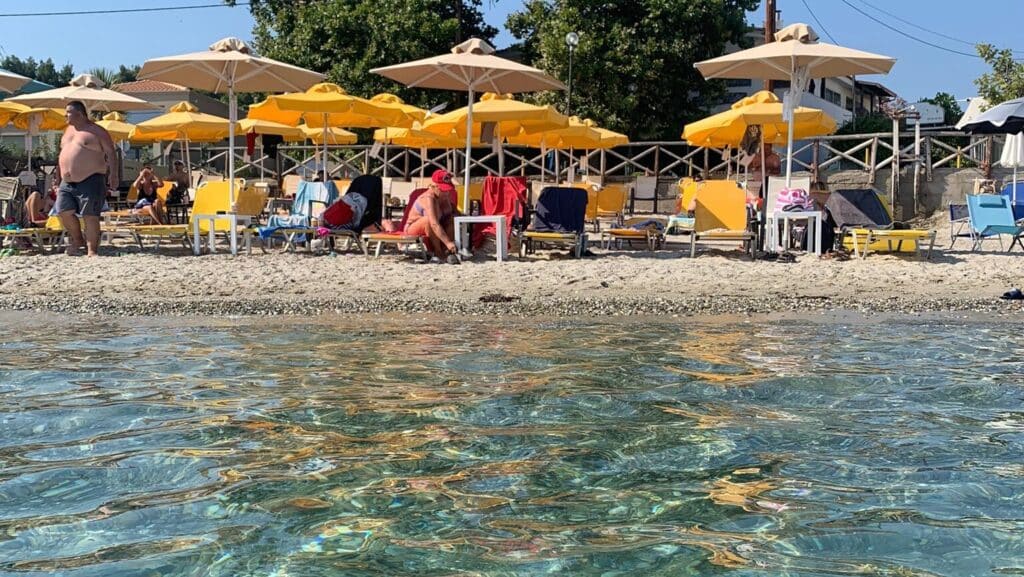 Yellow Parasols and sunbathers fill a small beach area in Greece.