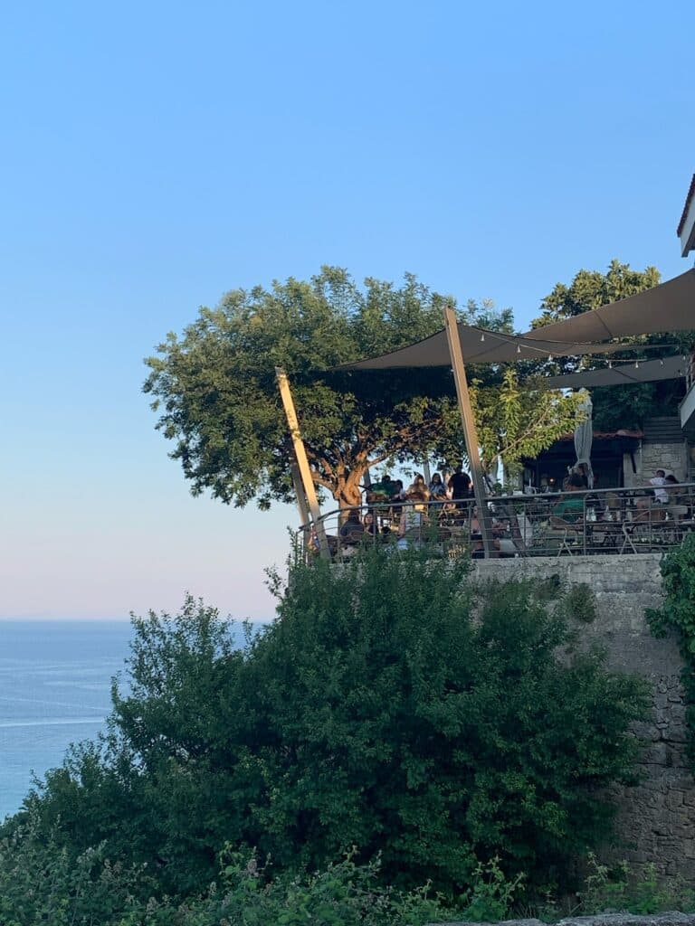 A restaurant overhangs the coastal cliffs with shrubs and trees surrounding it.