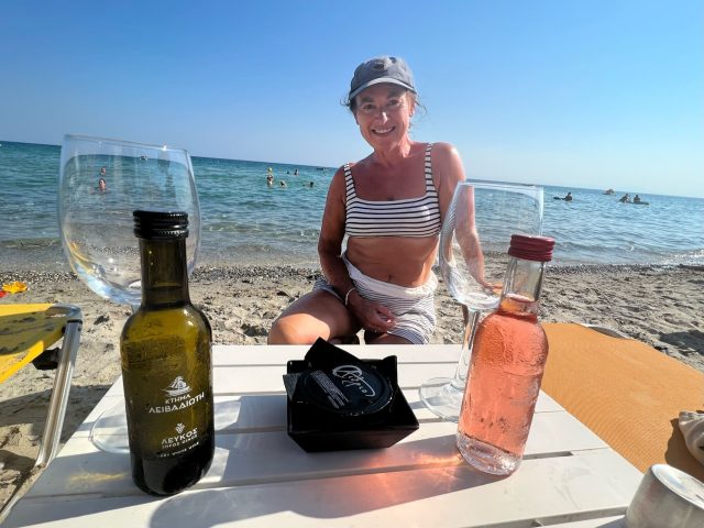Woman enjoying a break at a beach. She has her sunscreen and some wine.