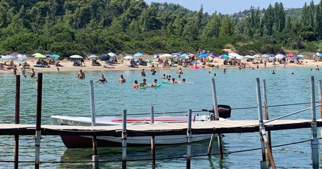 A boat is moored at a wooden jetty, next to a beach in Halkidiki Greece.