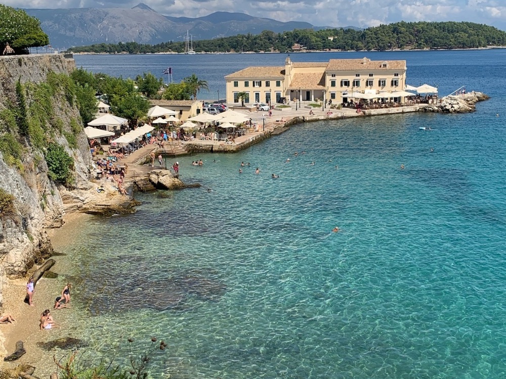 Shallow turquoise waters lap against a small harbour and town on the Greek island of Corfu.