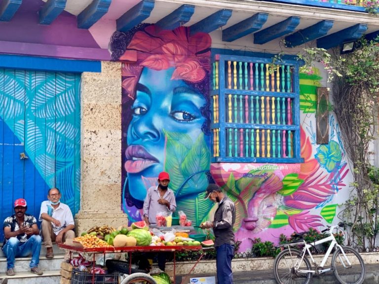 A fruit stall on a street in Cartagena with street graffiti art on the wall behind the cart.