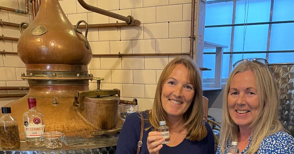 Two women enjoying a gin tasting standing next to one of the distilling stills.