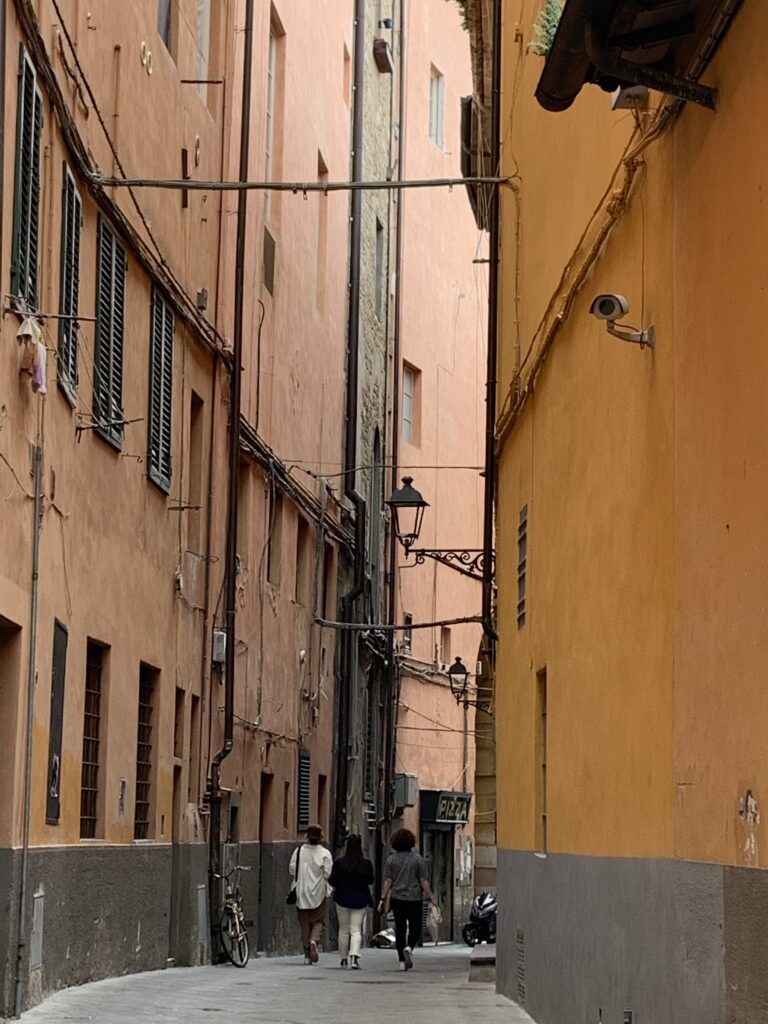 People walking through a tall narrow winding street in Pisa.