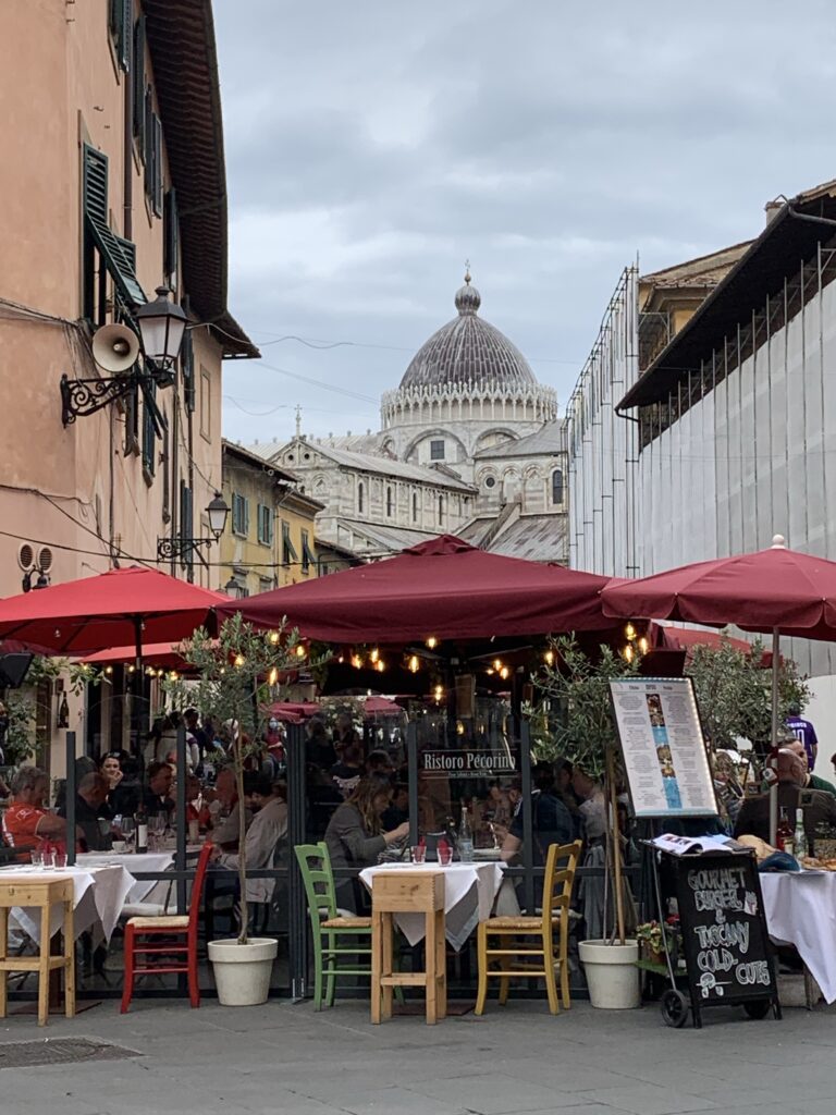 Dining al fresco in Pisa with red umbrellas shading diners.