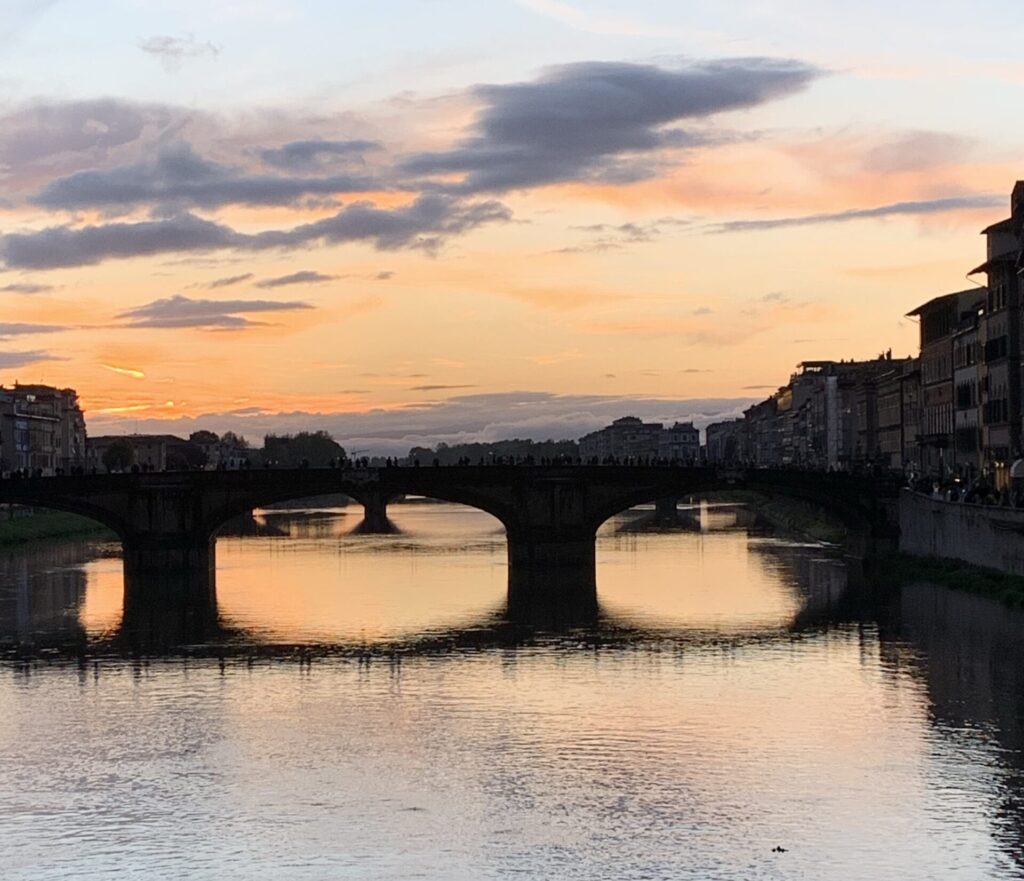 Sunset over a bridge in Florence, Italy. The sky is pink, orange and yellow with blue and grey.