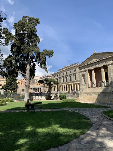 A garden with grass and large trees and behind a large column style building, operating as a museum.