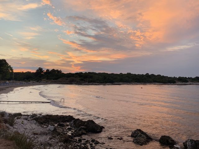 Sunset over a beach with pinks and blues in the sky between clouds.