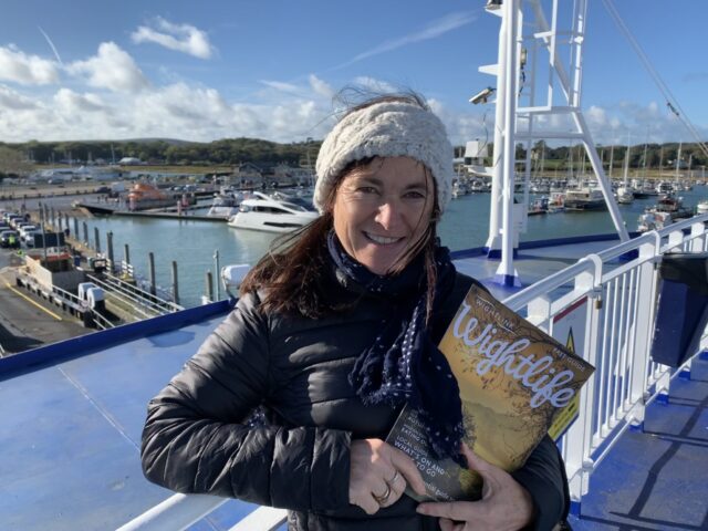A woman is on a ferry heading to the Isle of Wight. She is holding a travel brochure.