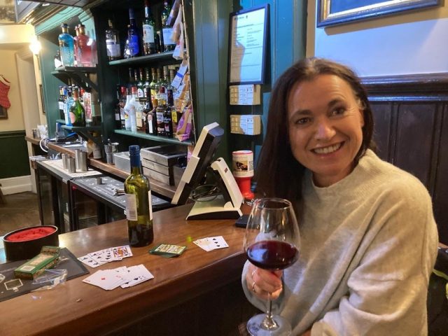 Woman is enjoying a glass of red wine inside a traditional English pub.