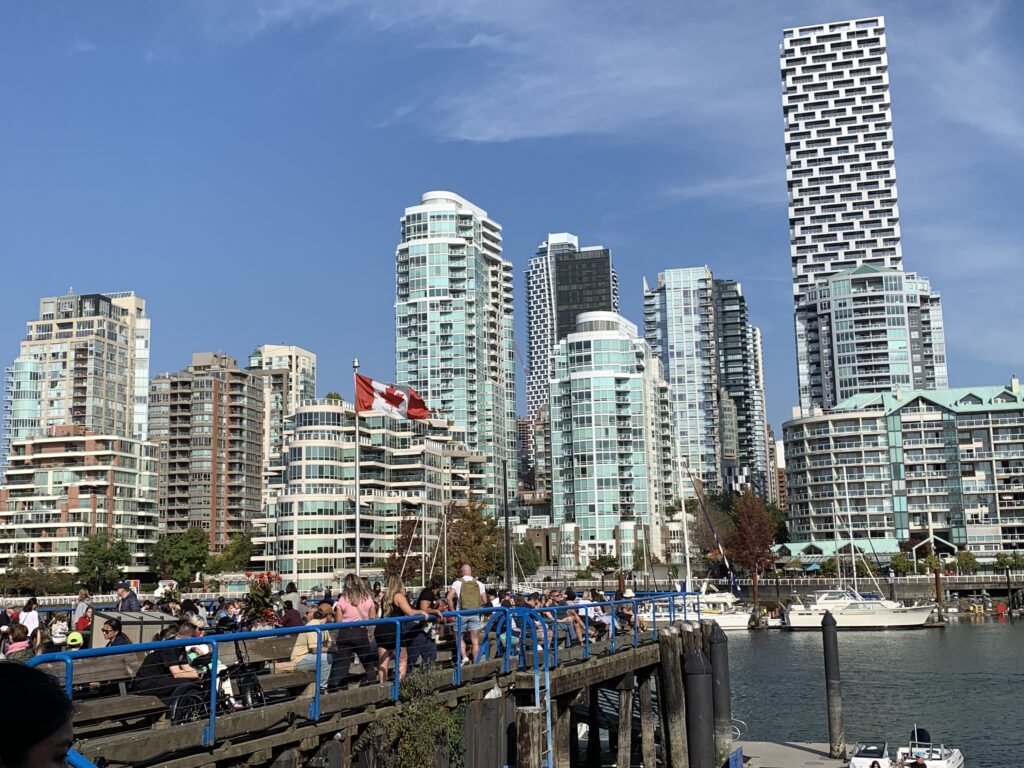 Skyscrapers with glass windows frame the sky of Vancouver. Sail boats sit in the harbor in front.