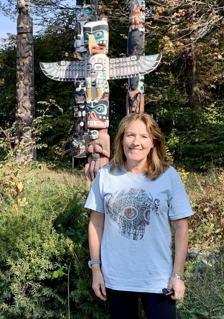 Woman in Stanley Park Vancouver standing next to a totem pole.