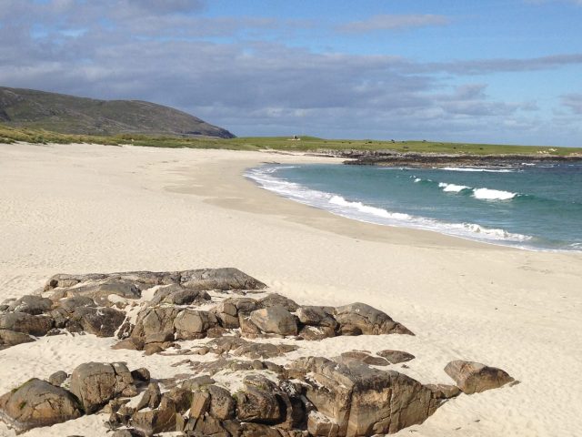Remote beaches with white sands and blue waters lapping the shore. Large rocks lay on part of the beach.