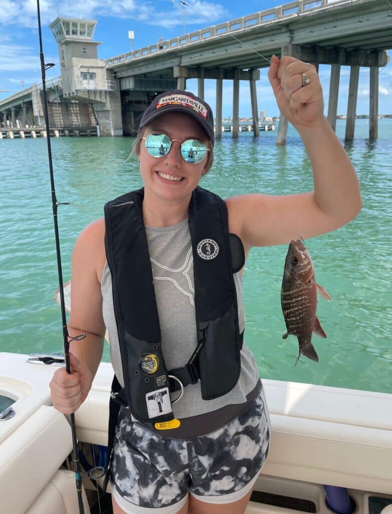 A woman is holding a small fish she caught fishing off a boat.