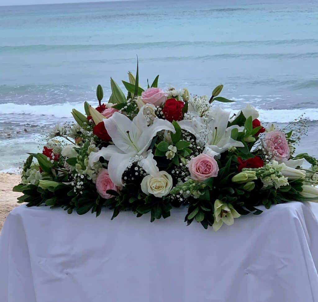 A wedding bouquet with red, pink and white flowers and green leaves.