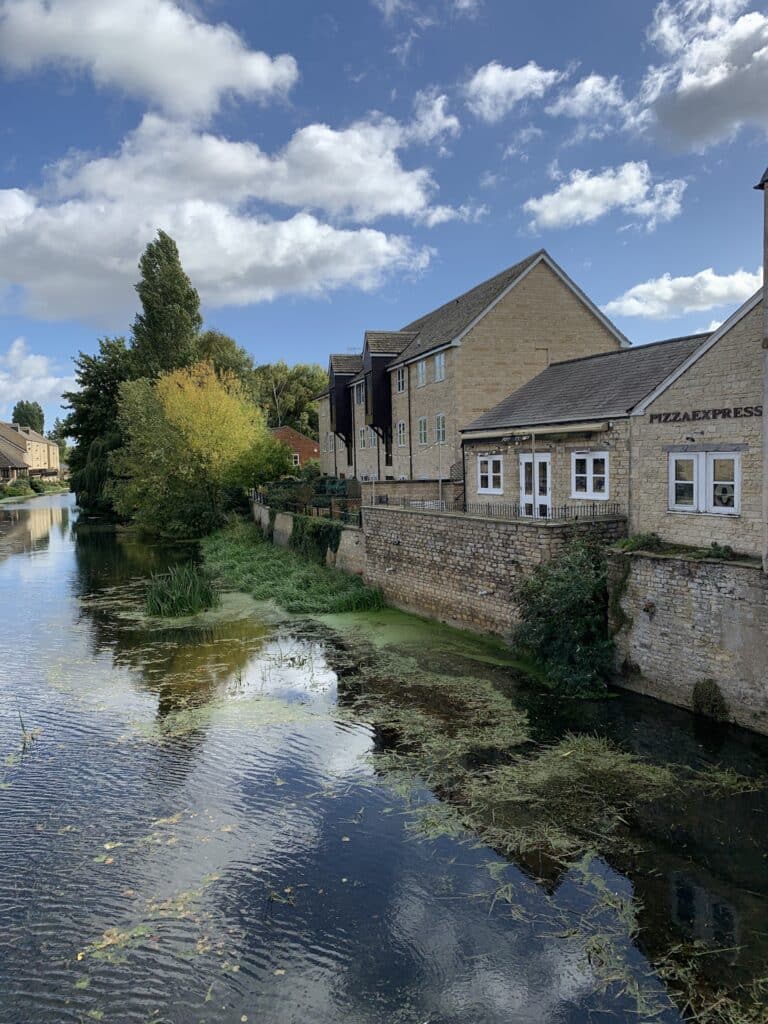 A river runs past a small town with homes separated by a stone wall.