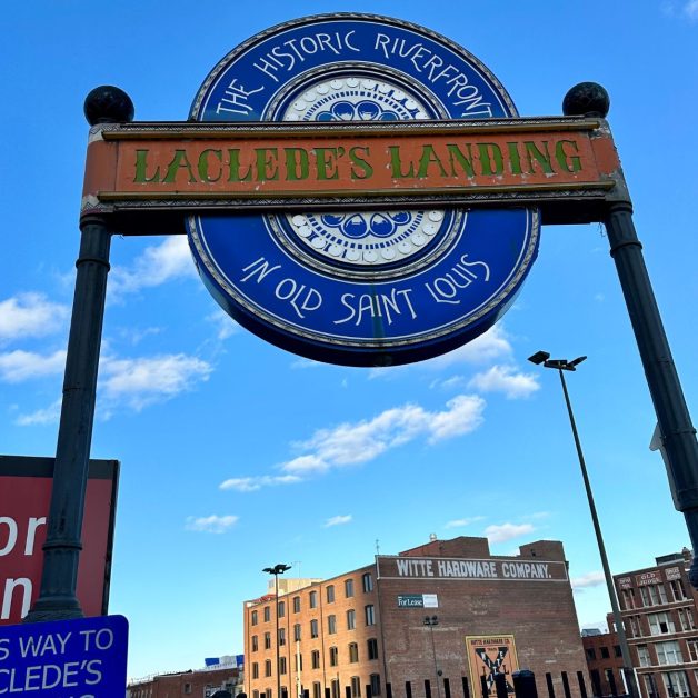A large blue circular sign for Lacledes's Landing in St Louis guides people to the riverwalk.