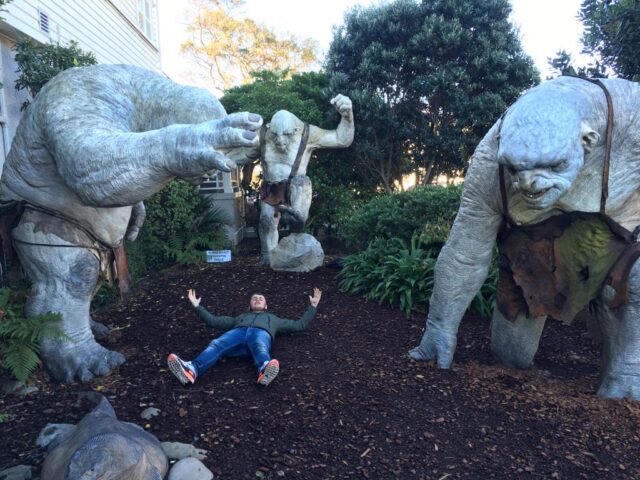A man is lying between larger than life replicas of characters from Lord of the Rings. The films were partially filmed in this location in New Zealand