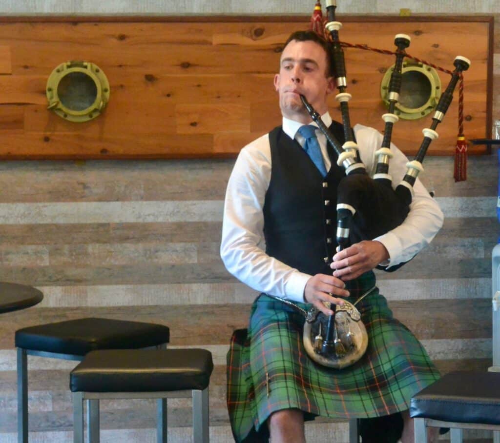 A man is playing the bagpipes and is wearing a kilt, a traditional Scottish garment.