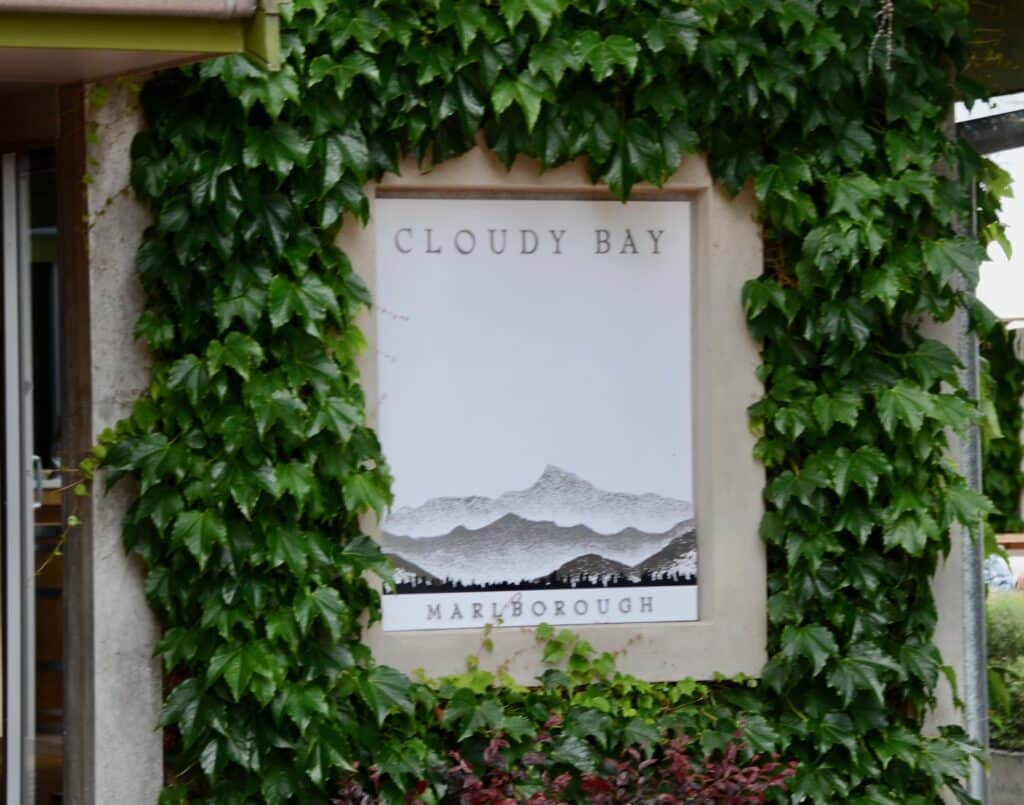 A sign in concrete and marble for a famous winery in New Zealand called Cloudy bay. Green Ivy grows around the sign.