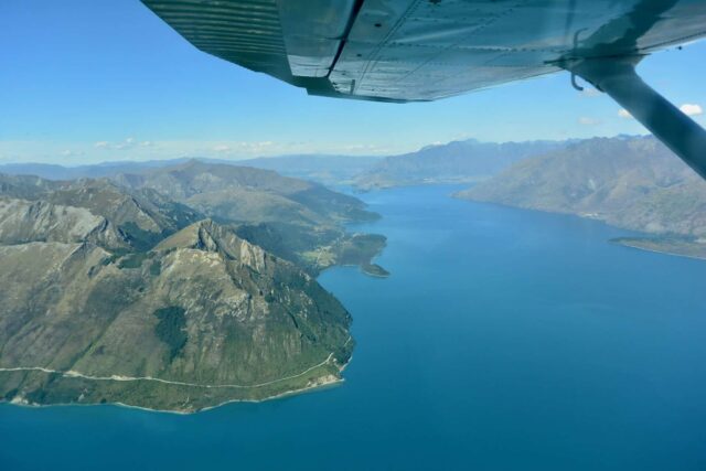 Fjords and mountains visible from a small plane. A small part of the wing of the plane is visible.