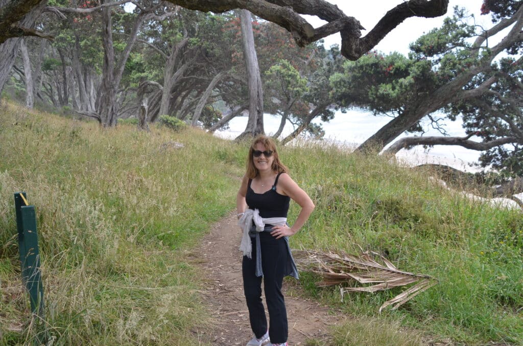 Hiker enjoying a coastal walk in the Coromandel Peninsular in New Zealand. There is a small dirt path to follow between forested areas.
