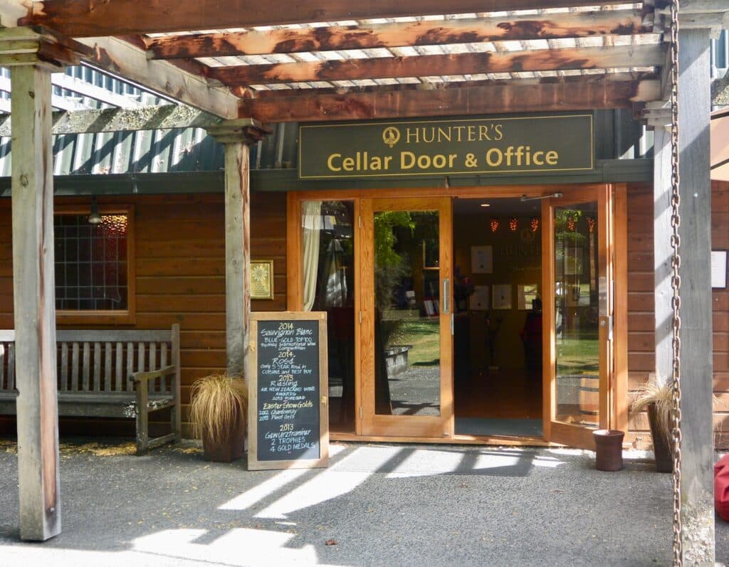 An entrance door made from wood and glass panels with a pagoda style entry for shade. The black board advertises wines and the name above the door says Hunters Wine Cellar.