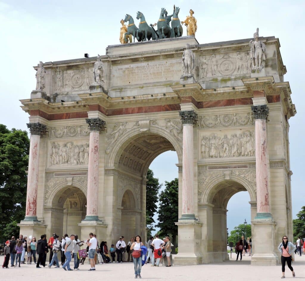 Three archways and columns are featured of the Arc de Triumph war memorials in Paris. On top of the statue are horses pulling a warrior in a chariot.