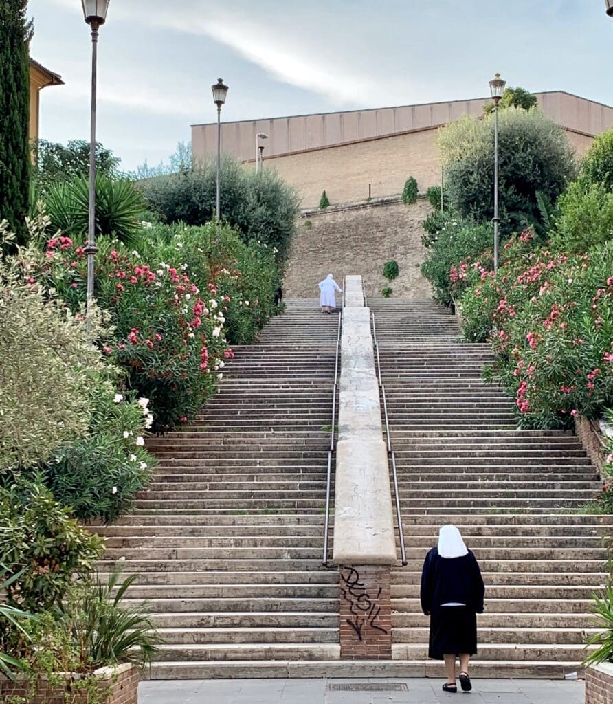A nun walks up a set of stairs towards the Vatican City.