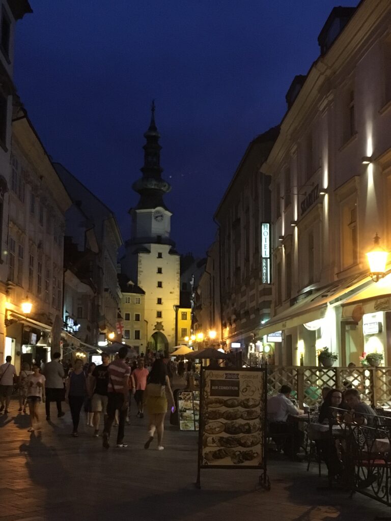 Street in Bratislava at night with people enjoying dinner in outdoor restaurants.