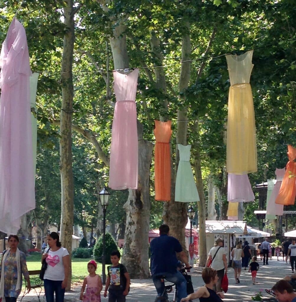 Different coloured dresses hang from trees in a park in Zagreb.