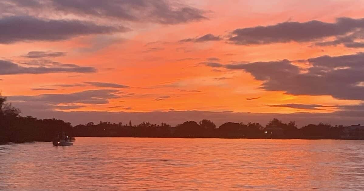 A sunset in Florida is one of our dream getaway destinations. The water is orange as the sinking sun reflects through the clouds.