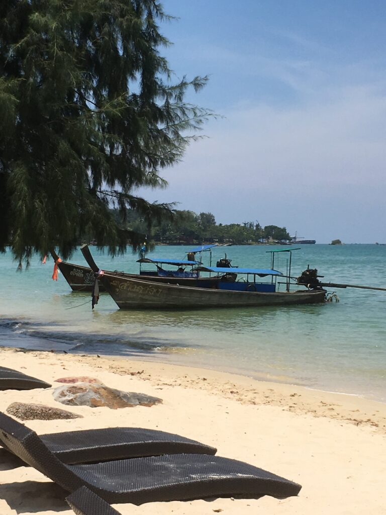 Beach with two small wooden boats tied up. The beach sands are soft yellow and trees are growing along the edge of the beach.
