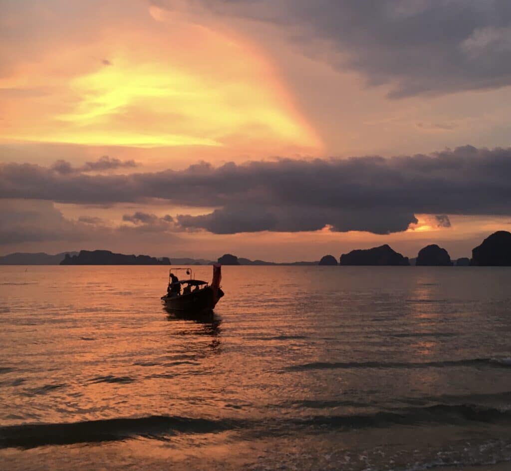 Sunset over the waters of Krabi, with a traditional boat sitting just offshore.