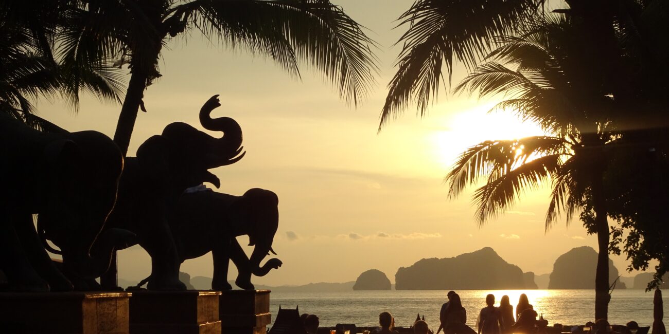 A group of people are watching the sunset. They are looking out to the outline of mountains on other islands in the distance.