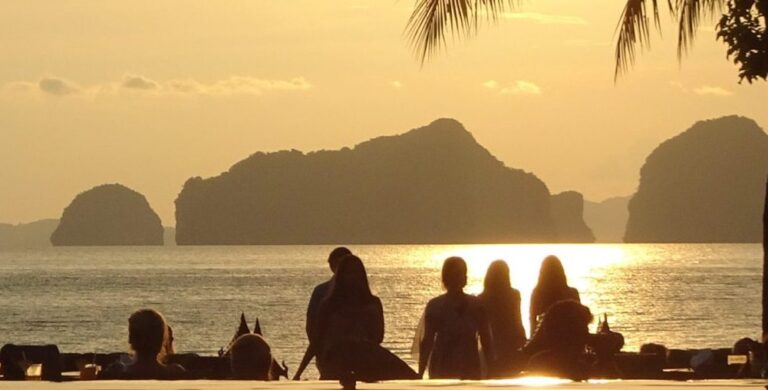 A group of people are watching the sunset. They are looking out to the outline of mountains on other islands in the distance.