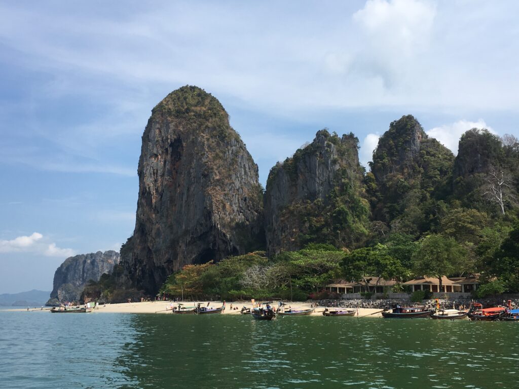 A cave and beach structure with 4 large stone peaks jutting out of the ground behind a beach with a sandy cove.