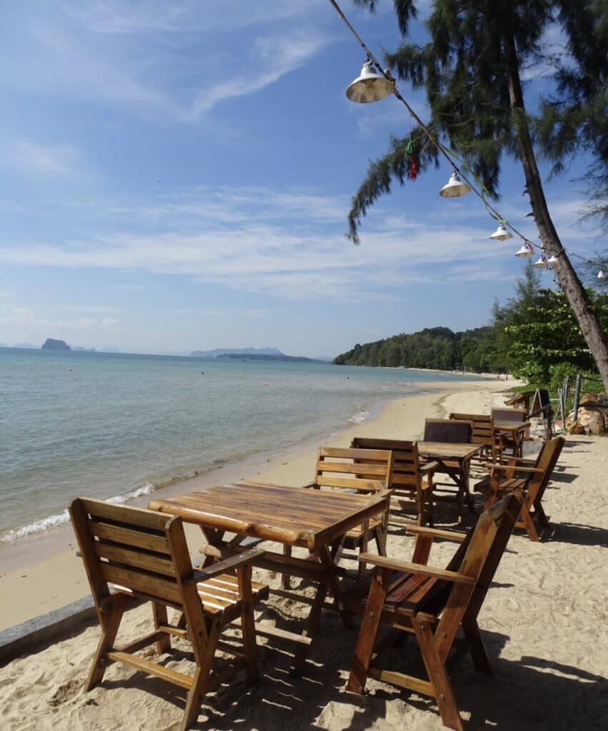 Wooden square tables and chairs set out on a beach in Krabi, Thailand