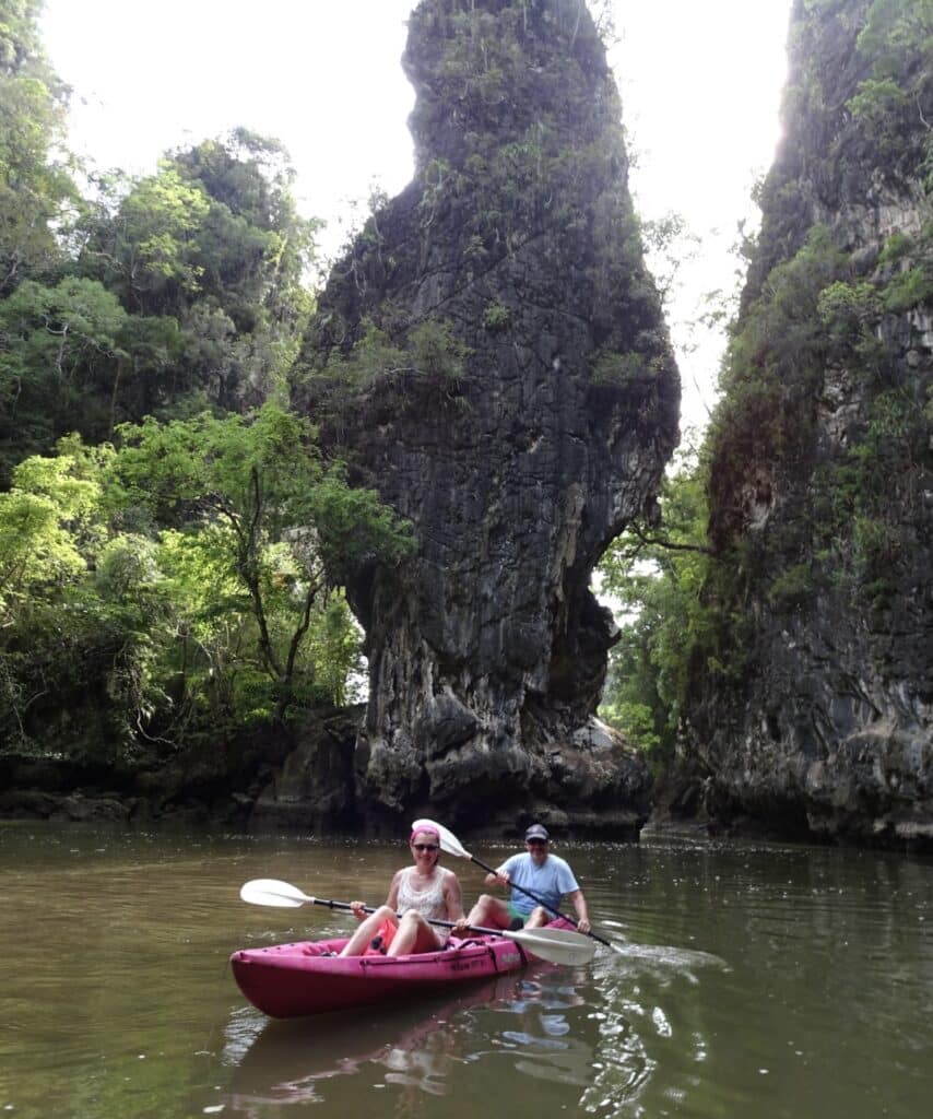 A couple is Kayaking around large rock formations near Krabi