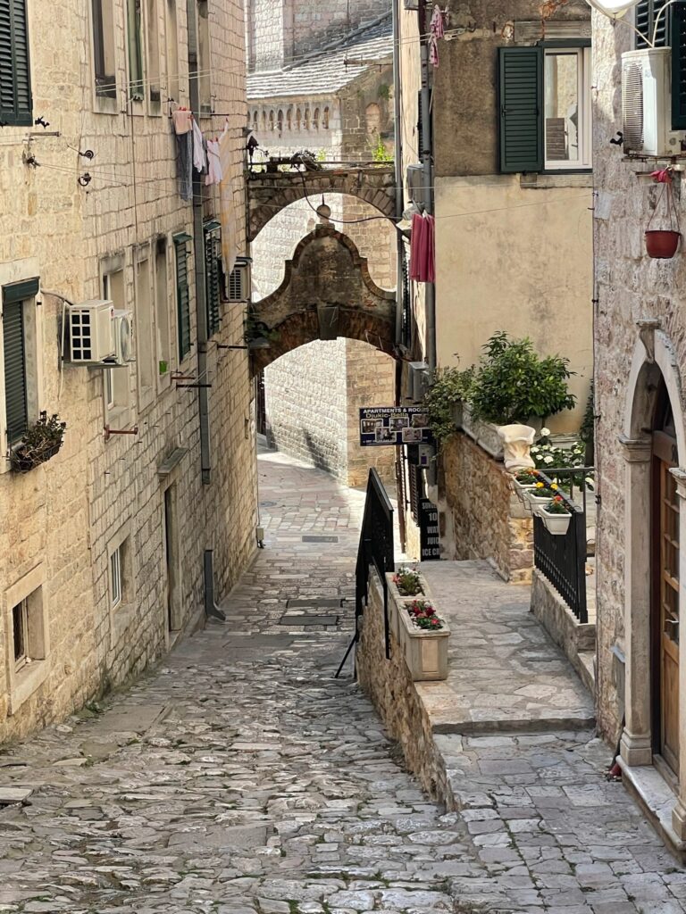 A cobbled street in a coastal town in Montenegro with low arches between narrow street walls.