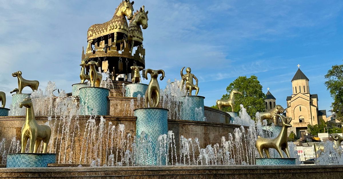 Alarge Fountain with golden figures from Georgian (Country) culture including 2 Large Gold Horses, Tamada figure and Rams all in gold sit atop blue tiled stands.