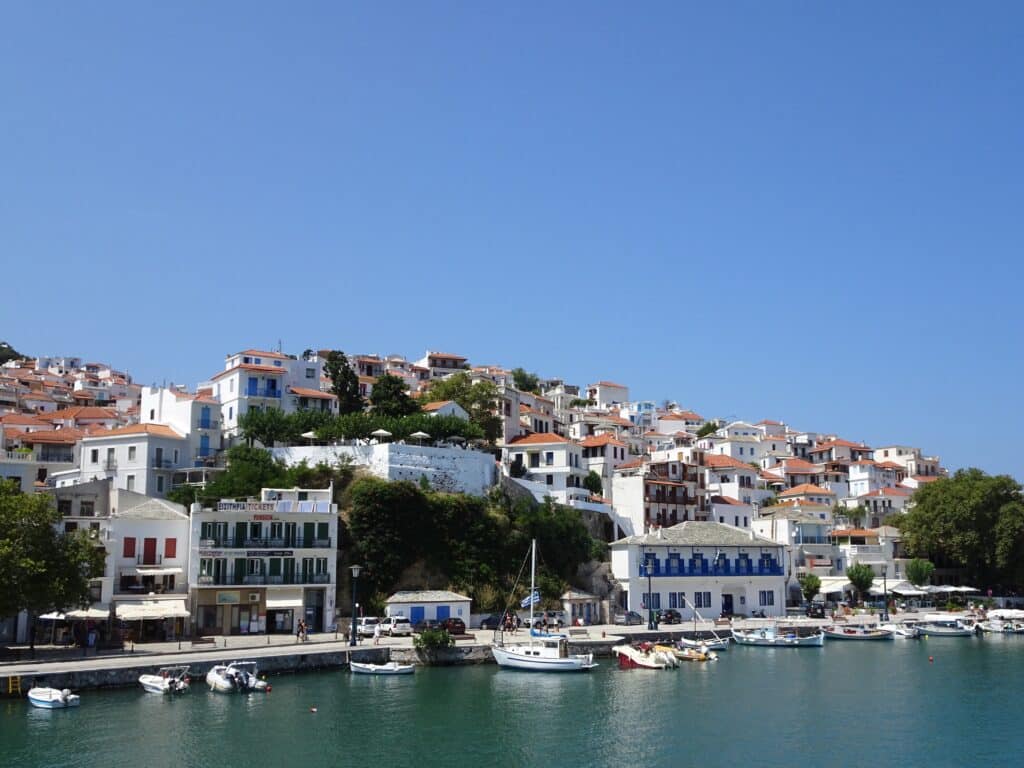 Greek island shore with hotels, homes and small boats moored by the small harbor wall.