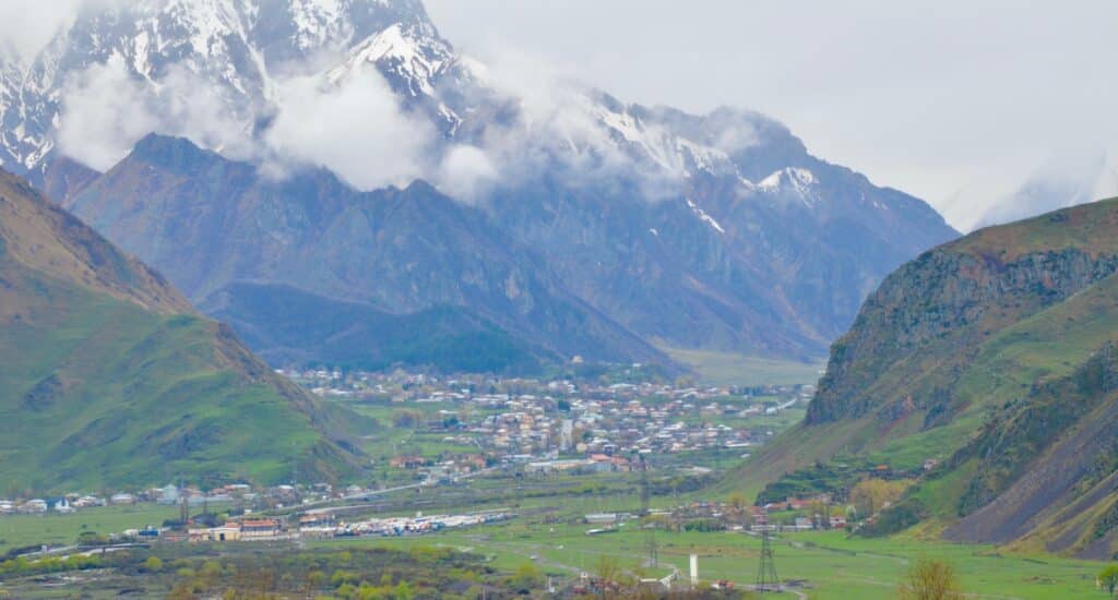 View of Kazbek Mountain with snow capped peaks and a town in the valley below.