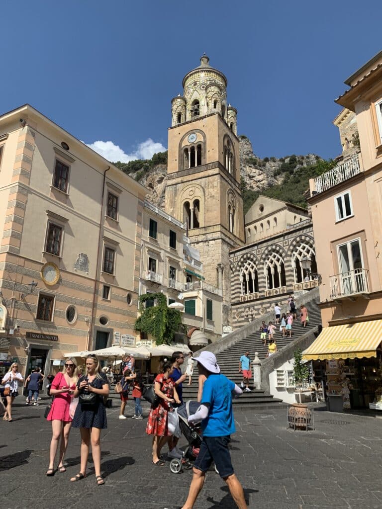 A small square in Amalfi Coast town Italy. People are walking around and old stone buildings surround the area.