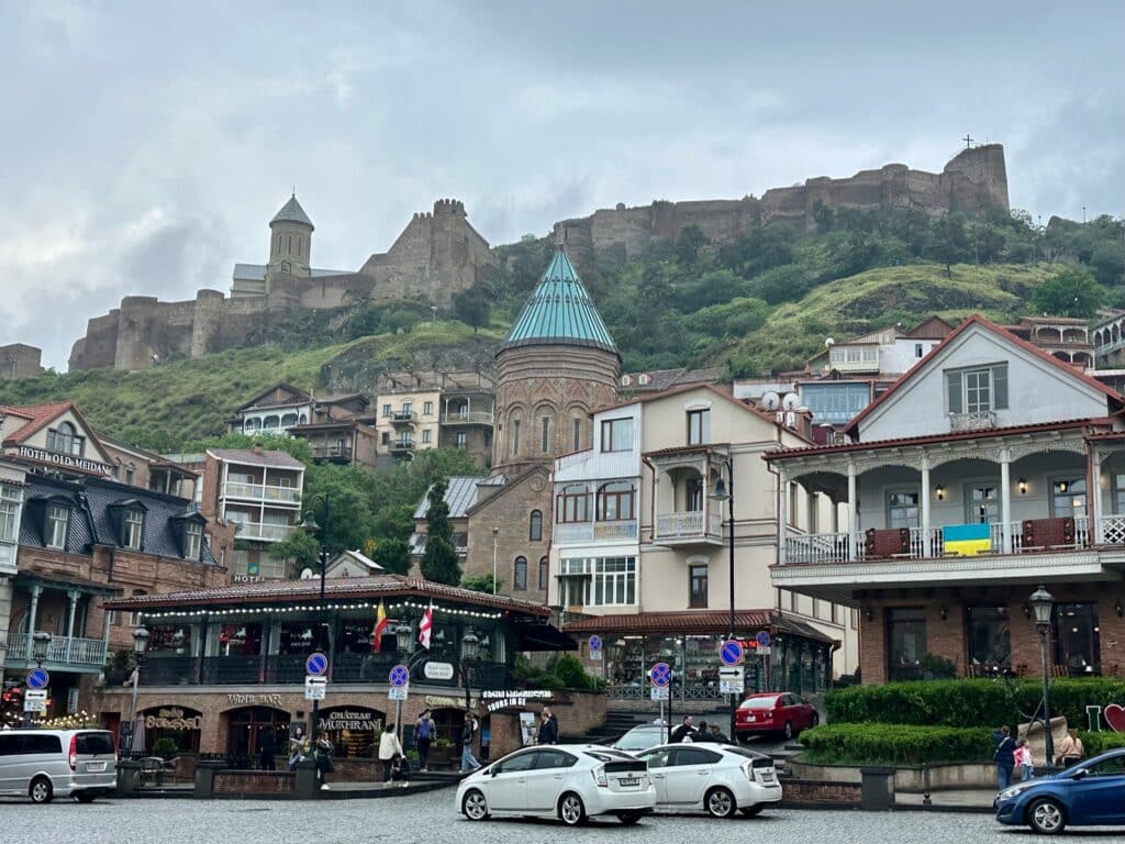 A street in Tbilisi Georgia showing a fortress on top of a hill behind the city center.