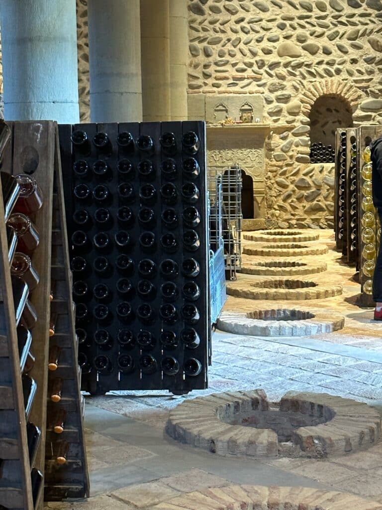 A wine cellar with round underground storage areas and racks of bottled wine.