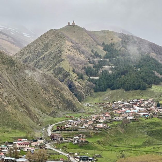 Gergeti Church and below it a small hamlet or village in the valley.