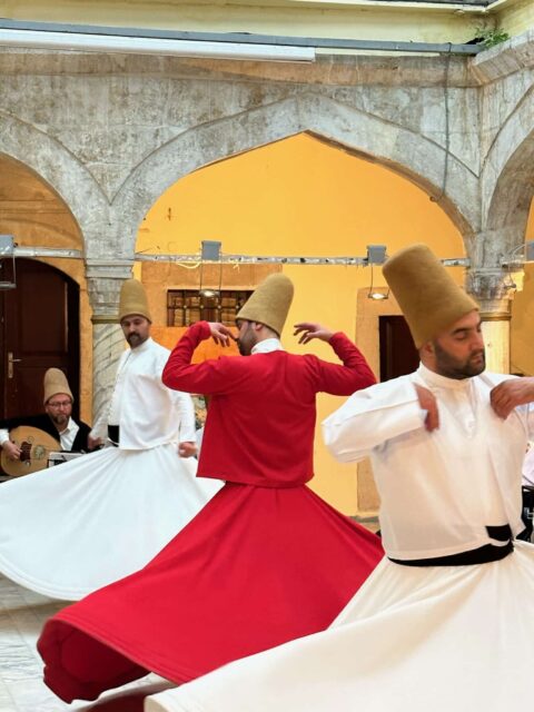 Whirling dervish Istanbul. Men in white and red clothes with brown felt hats turn in circles with closed eyes.